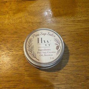 May include: A small, round, silver tin with a brown label that reads "Pine Sap Salve" and "HW" in a stylized font. The label also lists the ingredients: "Pine Sap, Coconut Oil, Beeswax" and the size: "2 oz".