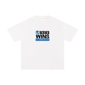 May include: White t-shirt featuring the text "1010 WINS" in black and blue, with a globe graphic. Below the text is "ALL NEWS 92.3 FM" in blue. The shirt has a relaxed fit.
