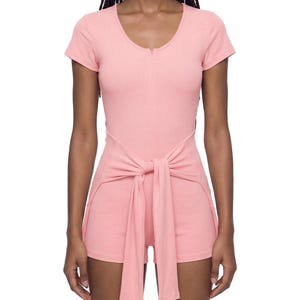 May include: A light pink romper with a tie-waist detail. The romper features a scoop neckline, short sleeves, and a zip-up front. The shorts are attached to the top, and the tie-waist adds a stylish touch to the outfit.