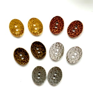 May include: Assortment of ten oval-shaped buttons in various metallic finishes, including gold, silver, copper, and bronze. Each button has two holes and a hammered texture.