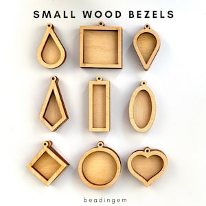 Peut inclure: Neuf petites lunettes en bois non finies de différentes formes, dont goutte d'eau, carré et cœur. Les lunettes sont brun clair et ont un petit trou en haut pour les suspendre. Le texte "SMALL WOOD BEZELS" est en haut et "beadingem" en bas.