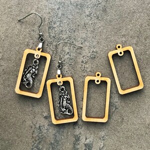 May include: Three pairs of wooden earrings with silver mermaid charms. The earrings are rectangular and have a simple design.