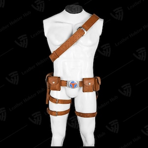 May include: Brown leather utility belt and harness set. The set includes a shoulder strap, belt with pouches, and leg straps. The belt buckle has a blue and orange design. The set is displayed on a white mannequin.