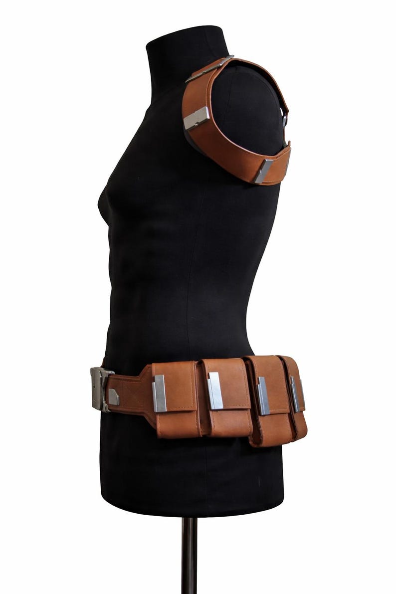 May include: Brown leather shoulder strap and belt set with silver-colored metal accents. The belt features three pouches. The set is displayed on a black mannequin.