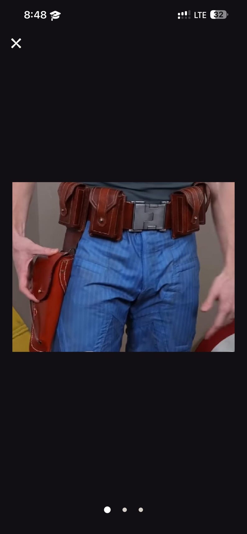 May include: A brown leather utility belt featuring multiple small pouches and a large holster attached to the side, worn over blue trousers with a subtle vertical stripe pattern. The belt is secured with a metallic rectangular buckle at the centre.