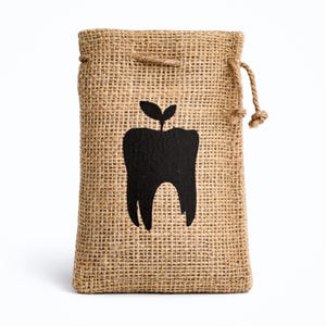 May include: A hessian drawstring bag featuring a black tooth design with a small plant sprouting from it. The bag has a natural, woven texture and a neutral colour. The bag is designed for small items.