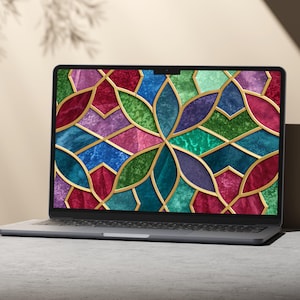 May include: A laptop computer displaying a colorful stained-glass design. The screen features a mosaic of jewel-toned shapes in red, blue, green, and purple, outlined with gold. The laptop is open on a light gray surface.
