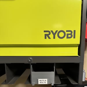May include: A lime green RYOBI storage cabinet with a dark gray frame. The cabinet has a lock and a label that reads "NUTS & BOLTS". The cabinet is designed for storing small hardware items.