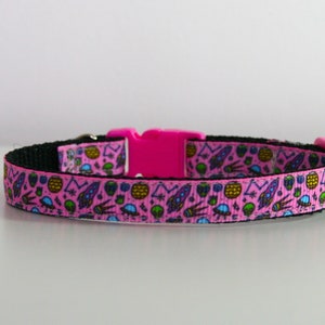 May include: Pink cat collar with a black buckle and a colorful pattern of rockets, aliens, and stars.