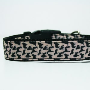 May include: A black and pink dog collar with a repeating pattern of black silhouettes of dogs. The collar has a black plastic buckle and a silver metal D-ring.