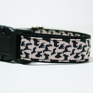 May include: A black dog silhouette pattern on a pink and black dog collar with a black plastic buckle.