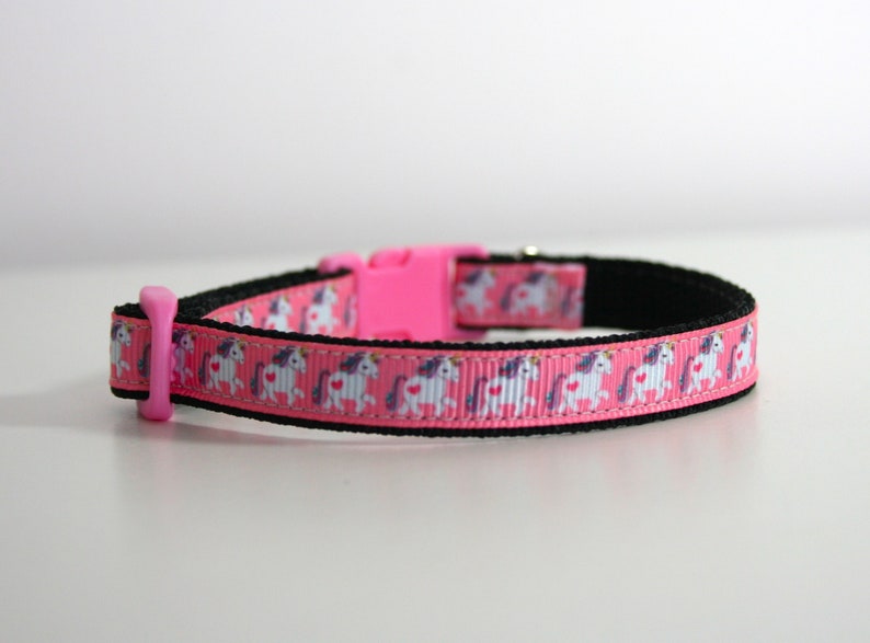 May include: Pink pet collar with a black buckle and a white unicorn pattern.