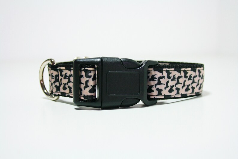 May include: A pink and black dog collar with a black plastic buckle. The collar is decorated with a repeating pattern of black dog silhouettes.