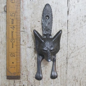 May include: A dark grey metal fox-shaped door knocker. The knocker has a detailed fox head with pointed ears and a textured finish. The knocker is approximately 15 cm tall and includes a ruler for scale.