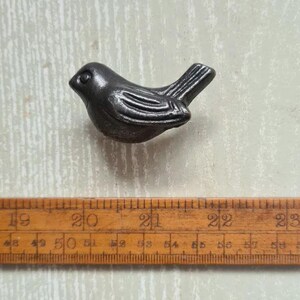 May include: A dark grey, bird-shaped metal knob or decorative pull. The bird is depicted in profile with moulded wing and tail feather details. It is positioned above a wooden ruler that shows a length of approximately 10 centimetres for the bird.
