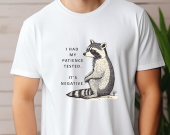 May include: White t-shirt with a black and white illustration of a raccoon. The text on the shirt reads "I had my patience tested. It's negative."