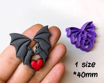 May include: A digital STL file for a clay cutter for earrings, featuring a purple plastic cutter and a black clay shape of two bats facing each other with a red heart between them. The text reads DIGITAL STL FILE, 1 size, 40mm, CLAY CUTTER FOR EARRING.