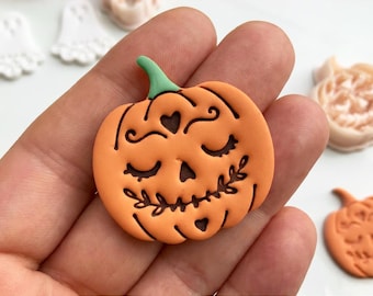 May include: An orange pumpkin-shaped clay cutter with a green stem, featuring engraved details of closed eyes, a heart-shaped nose, and a leafy mouth. The text DIGITAL STL FILE and CLAY CUTTER FOR EARRING are visible at the top and bottom.