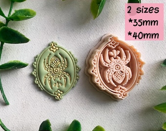 May include: A digital STL file for a clay cutter for earrings, featuring a spider design in an oval frame. The set includes two sizes, 35mm and 40mm. The image shows a light green pressed clay piece with a gold spider and a peach-colored cutter.