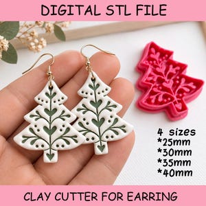Könnte beinhalten: Ein Paar weiß-salbeigrüne Weihnachtsbaum-Ohrringe mit goldfarbenen Haken und ein rosa Kunststoff-Ausstecher. Text: DIGITAL STL FILE, 4 sizes *25mm *30mm *35mm *40mm, CLAY CUTTER FOR EARRING. Das Tannenbaum-Design zeigt eingearbeitete Herzmotive.