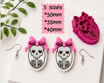 May include: A digital STL file for a clay cutter for earrings, featuring a skeleton with heart-shaped eyes and a pink bow. The text reads: DIGITAL STL FILE, 3 sizes, 30mm, 35mm, 40mm, CLAY CUTTER FOR EARRING. Includes two finished earring charms and hooks.