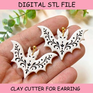 May include: A pair of white bat-shaped earrings featuring intricate black filigree patterns and gold-tone metal jump rings. The text DIGITAL STL FILE and CLAY CUTTER FOR EARRING is visible at the top and bottom of the image frame respectively.