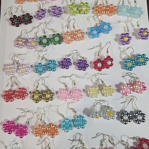 May include: A collection of colourful beaded flower earrings. The earrings are made with small, round beads in various colours, including pink, blue, green, yellow, red, and purple. The earrings are all in the shape of a flower with five petals.
