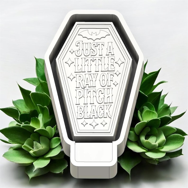 May include: A white coffin-shaped object with a flat top featuring the engraved text 'JUST A LITTLE RAY OF PITCH BLACK' and a small bat icon at the top. The design includes decorative star accents and clean, geometric lines throughout the surface.