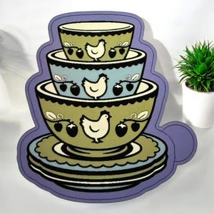 May include: A decorative stack of nesting bowls with a whimsical design. The bowls are in shades of green and blue, adorned with white chickens and red berries. The stack sits on a stack of plates, all outlined in a purple border.