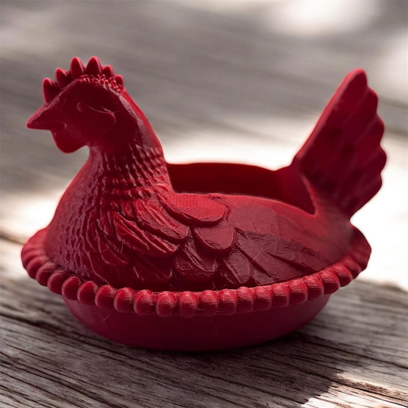 May include: A red, hen-shaped decorative container. The container is designed to resemble a hen sitting on a nest. The hen has detailed feathers, a comb, and a beak. The container is made of a solid material and is suitable for holding small items.