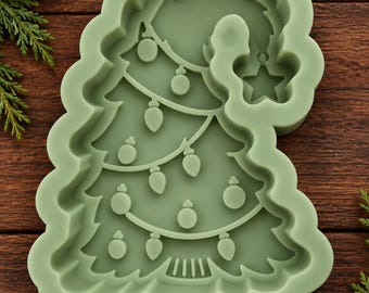 May include: A sage green silicone mold shaped like a Christmas tree with a curved top. The interior design features embossed details of a string of lights with round bulbs and a star at the very top, creating a recessed pattern for casting.