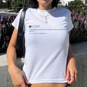 May include: White t-shirt featuring a Twitter post by John Summit: "unfortunately for my haters i will once again be living my best life this weekend." The post includes the time, date, and views. The shirt is worn by a person.