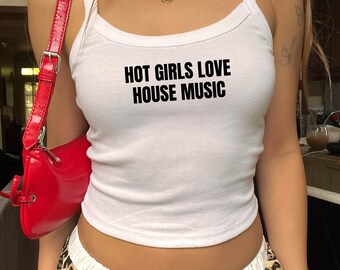Może przedstawiać: Biały top na ramiączkach z czarnym napisem "HOT GIRLS LOVE HOUSE MUSIC". Czerwona torebka przewieszona przez ramię. Osoba ma na sobie spódnicę w panterkę i złote naszyjniki.