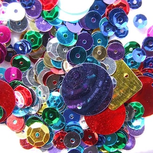May include: A collection of colourful sequins in various shapes and sizes. The sequins are in a variety of colours, including red, green, blue, purple, gold, and silver. The sequins are scattered across a white surface.