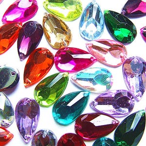 May include: A selection of teardrop-shaped rhinestones in a variety of colours, such as pink, purple, orange, green, and blue. Each gem has a faceted surface and a hole at the top for stringing or attaching. Ideal for jewellery making and crafts.