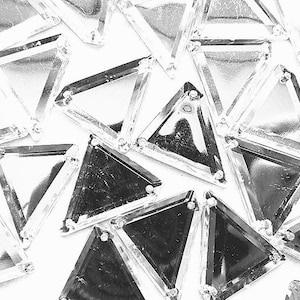 May include: A collection of clear, triangular rhinestones with a reflective, metallic appearance. Each rhinestone has a faceted design and is set with small, silver-coloured prongs. The rhinestones are scattered on a white surface.