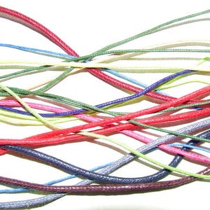 May include: A close-up of a collection of colourful cords in various shades, including red, blue, green, and purple. The cords are intertwined and arranged against a white background, creating a vibrant and textured display.