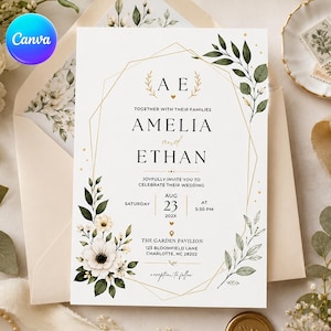 May include: A white wedding invitation card featuring a gold geometric frame, watercolor green leaves, and white flowers. The text reads Amelia and Ethan, August 23, 202X, at 5:30 PM, at The Garden Pavilion, 123 Bloomfield Lane, Charlotte, NC 28202.