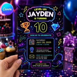 May include: A rectangular birthday invitation card with a black background and neon-style graphics including a trophy, diamond, arcade machine, and headphones. The text reads: Level Up! Jayden is turning 10. Join us to celebrate! Saturday July 26, 2025.