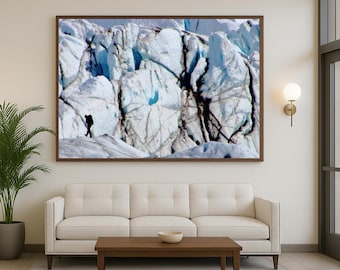 May include: A framed photograph of a glacier with a person silhouetted in the foreground. The glacier is a mix of white and blue hues, with dark cracks and crevices. The person is small in comparison to the massive ice formation.