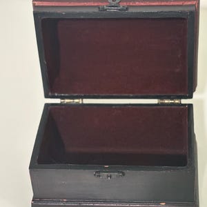 May include: A dark brown wooden box with a hinged lid, open to reveal a burgundy velvet interior. The top of the box is reddish-brown. A small metal clasp secures the lid. The box is designed for storing small items.