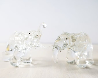 May include: Two clear glass elephant figurines. The elephants are facing each other and have their trunks raised.