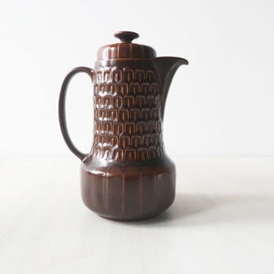 Peut inclure: Une cafetière en céramique brune avec un motif géométrique. La cafetière a un couvercle et une poignée.