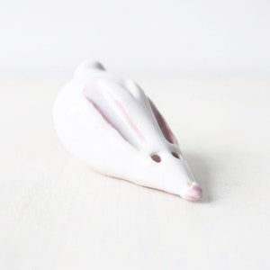 May include: A white ceramic rabbit figurine with pink accents. The rabbit is lying on its side with its head turned to the side.