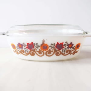 May include: White oval casserole dish with a glass lid. The dish has a floral pattern in shades of orange, brown, purple, and green.