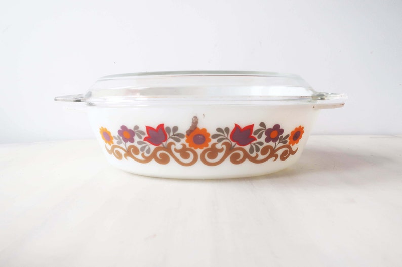 May include: White oval casserole dish with a glass lid. The dish has a floral pattern in shades of orange, brown, purple, and green.