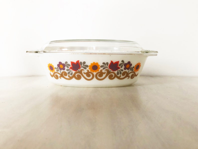 May include: White oval casserole dish with a glass lid. The dish has a floral pattern in shades of orange, brown, purple, and green.