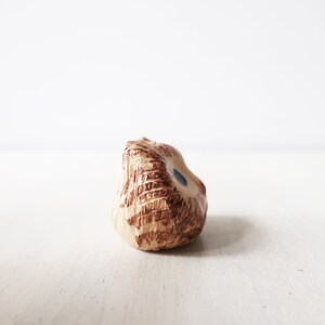 Op de afbeelding: Een kleine keramische uilfiguur in bruin- en beigetinten, met een textuur. De uil heeft een klein blauw oog en staat tegen een witte achtergrond.
