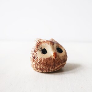 Op de afbeelding: Een kleine keramische uilfiguur met een bruin en beige getextureerd lichaam. De uil heeft grote zwarte ogen, een kleine oranje snavel en delicate wimpers. Decoratief item.