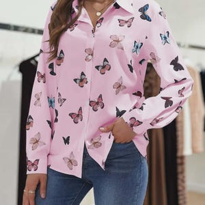 Peut inclure: Une chemise rose clair à boutons et manches longues, ornée d'un motif de papillons de différentes couleurs : rose, noir et bleu. La chemise est en tissu léger et possède un col classique.